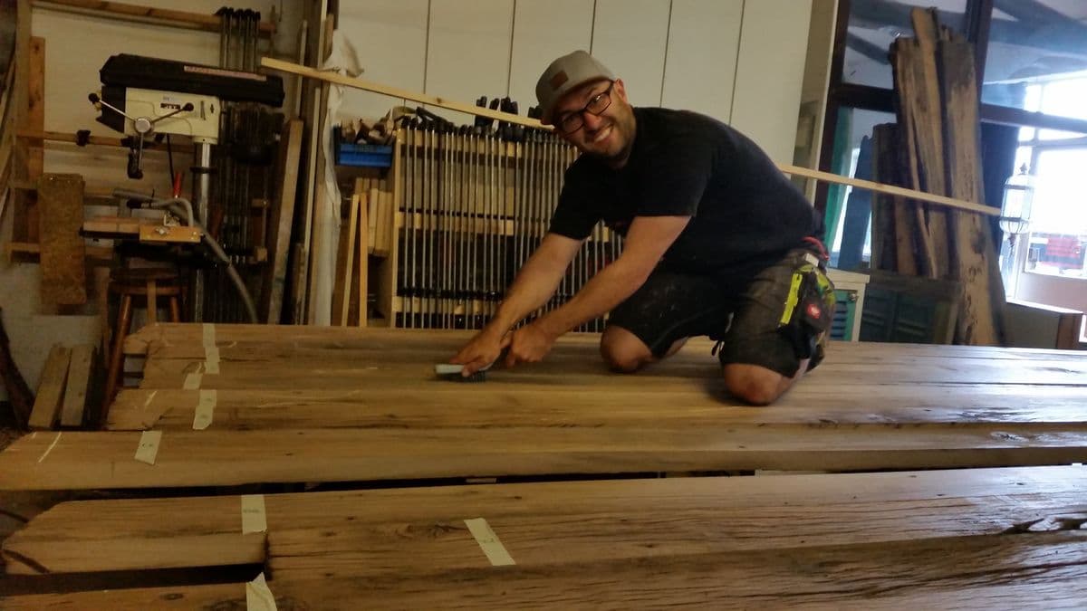 Milan Oesert in the carpentry workshop, kneeling at wood planks